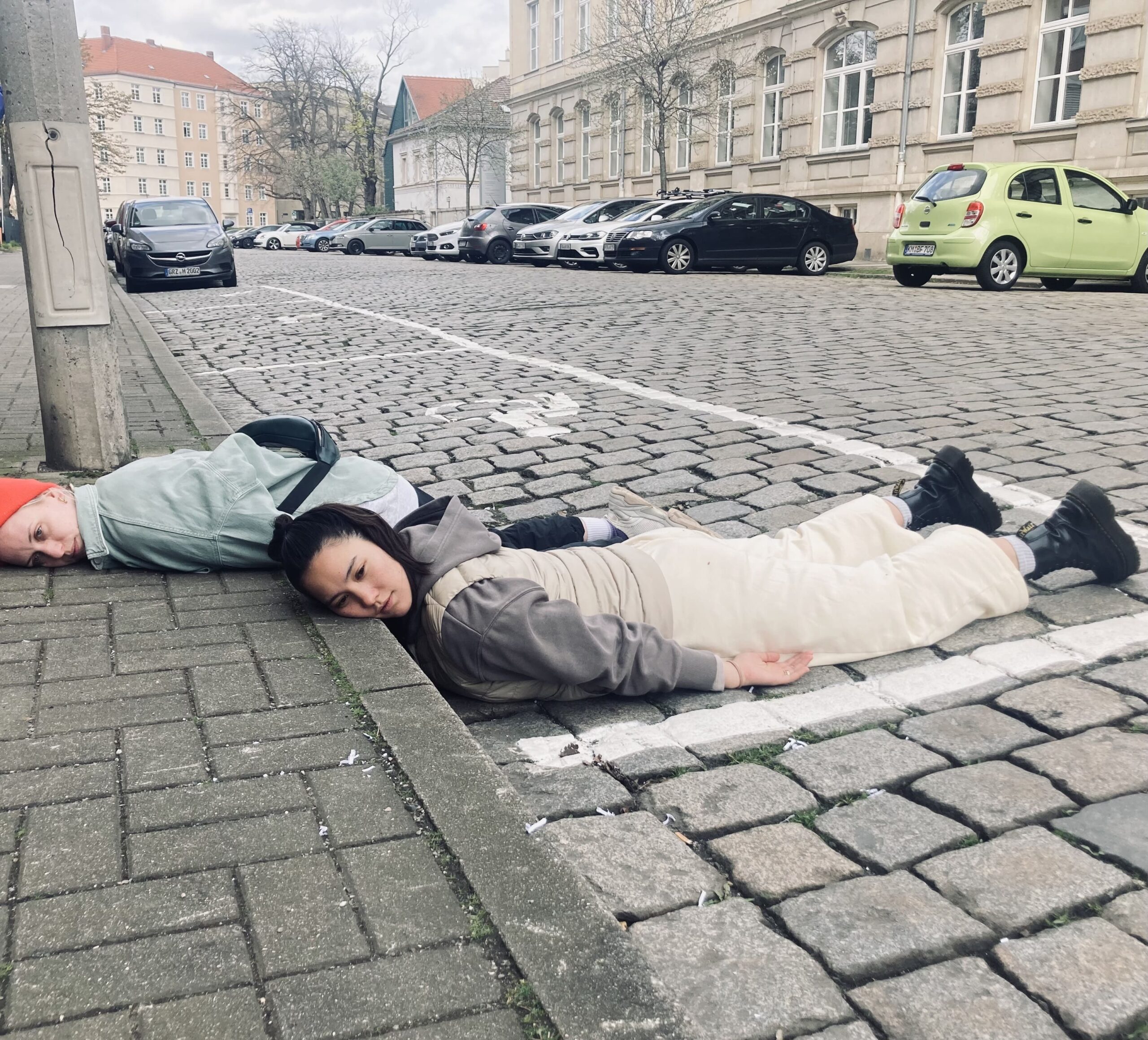 2 Menschen liegen in einer Parklücke auf Kopfsteinpfleastewr