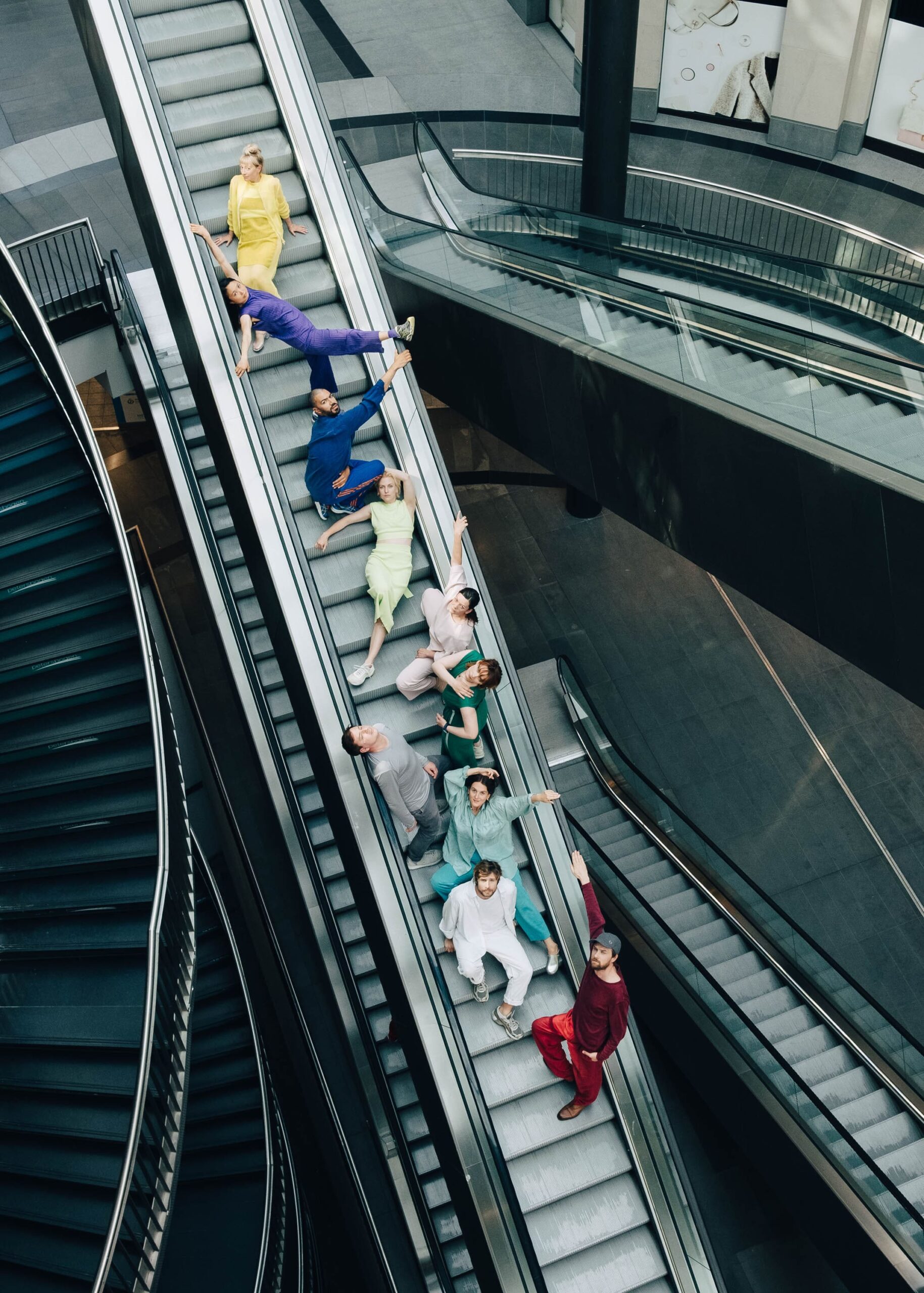 mehrere bunt gekleidete Menschen in interessanten Haltungen auf einer Rolltreppe