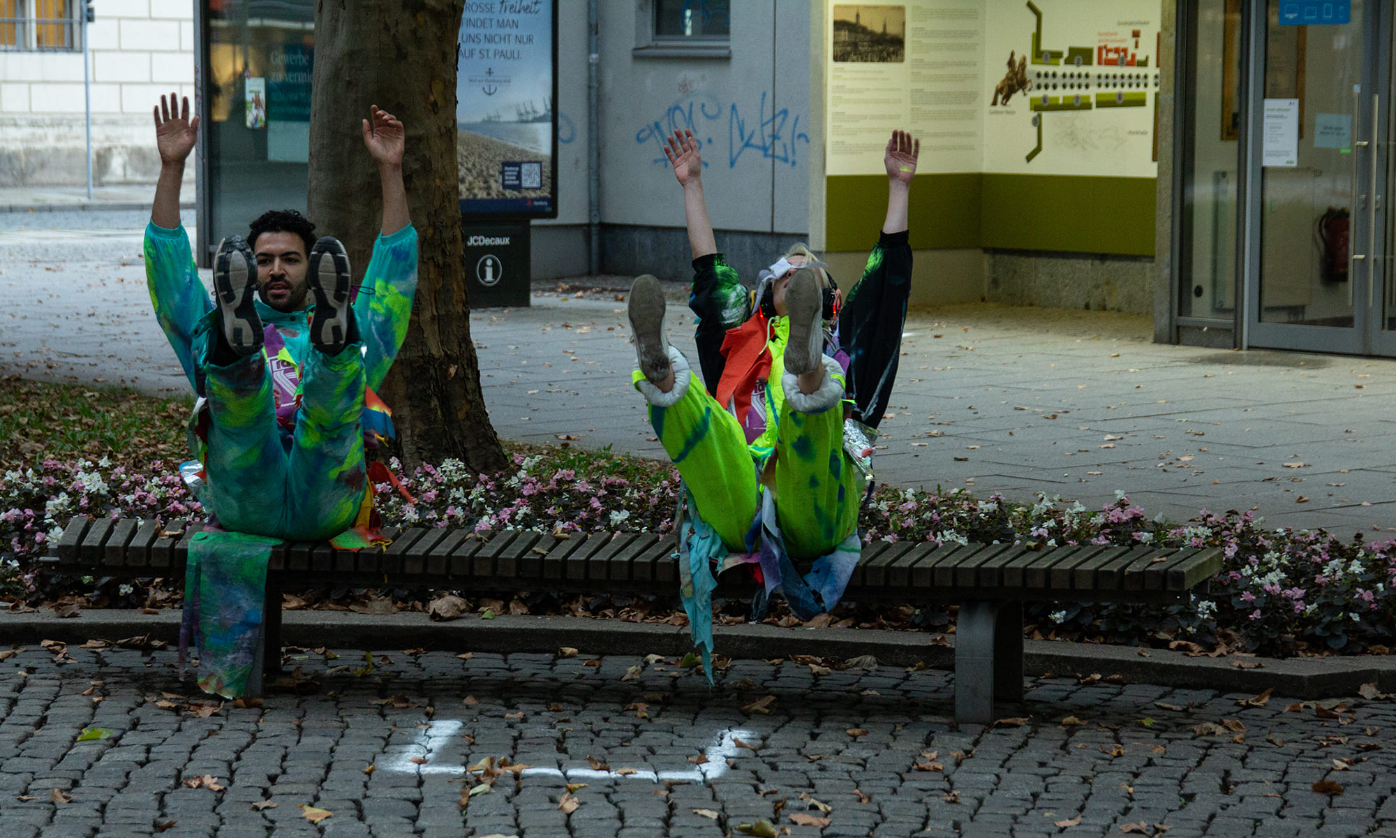 2 Manschen sitzen auf einem Bordstein und heben Arme und Beine