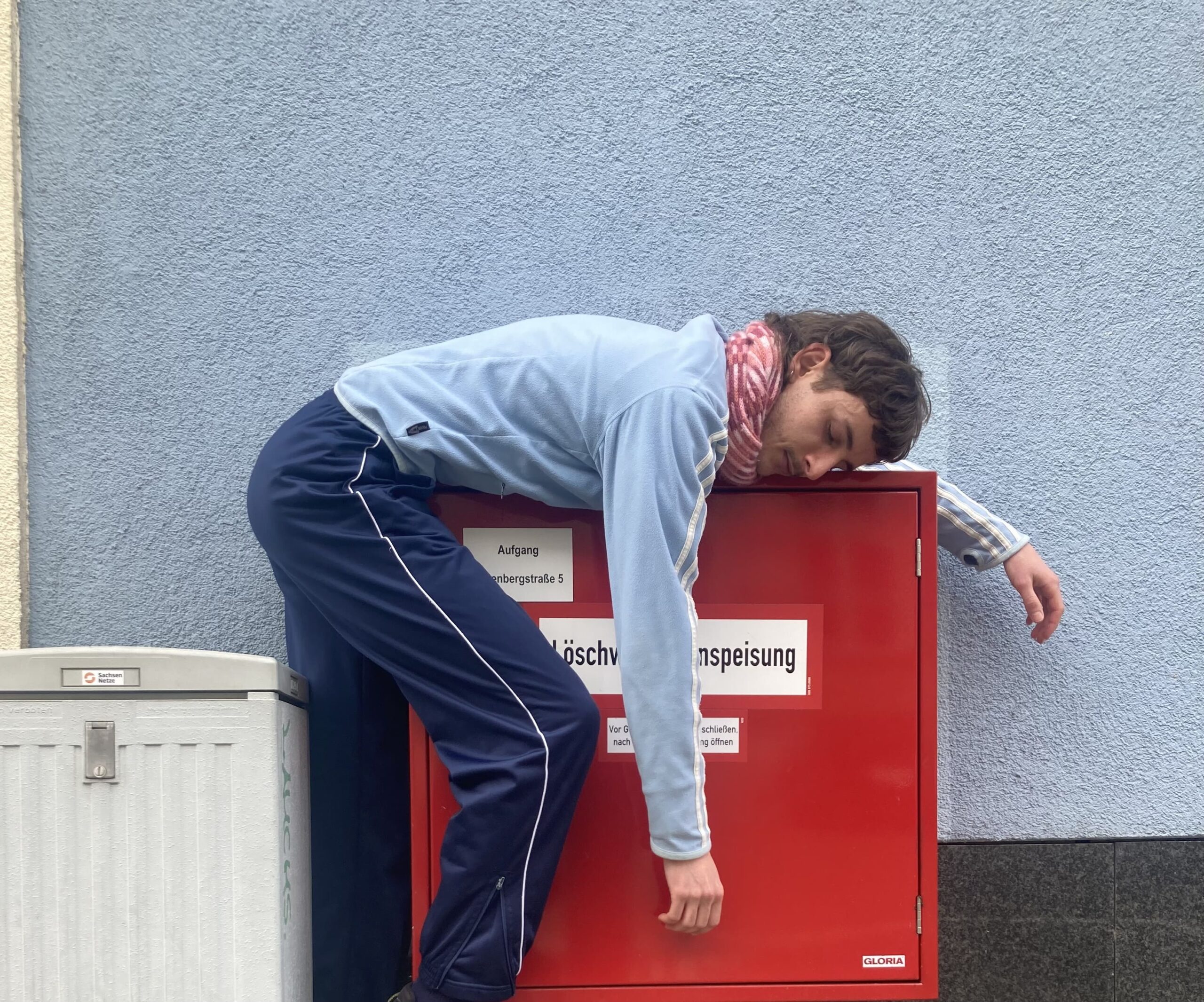 Person lehnt über einem roten Metallkasten mit der Aufschrift "Löschwassereinspeisung"