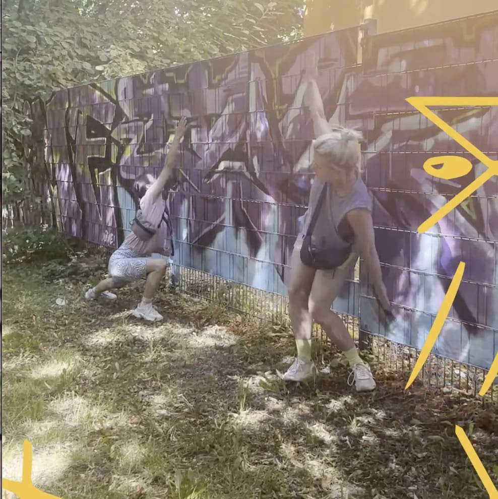 2 Menschen tanzen, angeschmiegt an eine mit Graffitti besprühte Wand