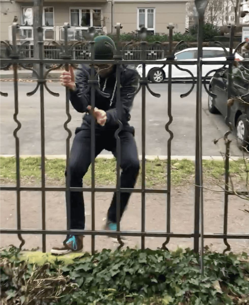 Junger Mann klettert an einem gusseisernen Zaun