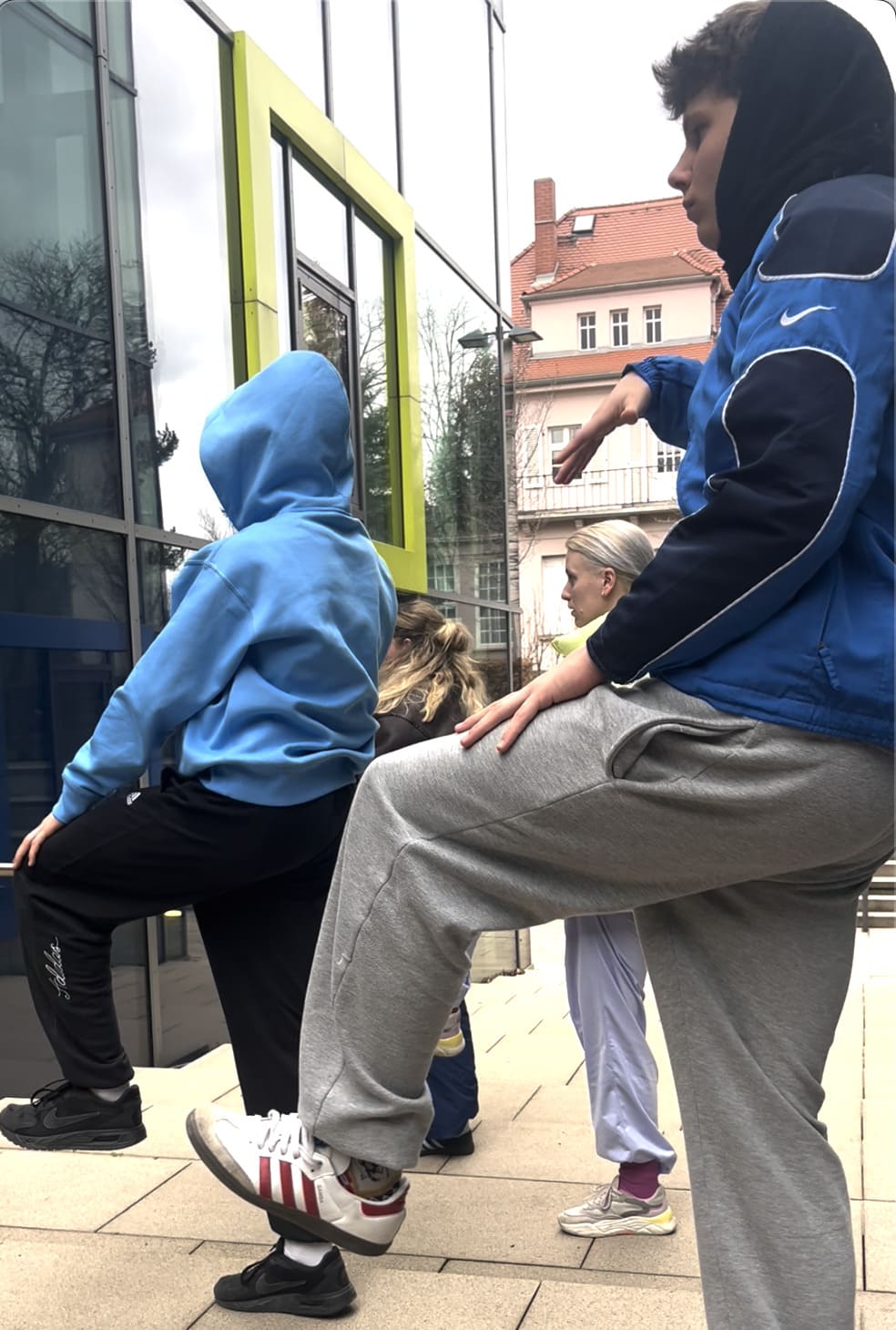 Junge Menschen in Pose auf einem Bein vor dem Glasgebäude der Palucca Hochschule Dresden
