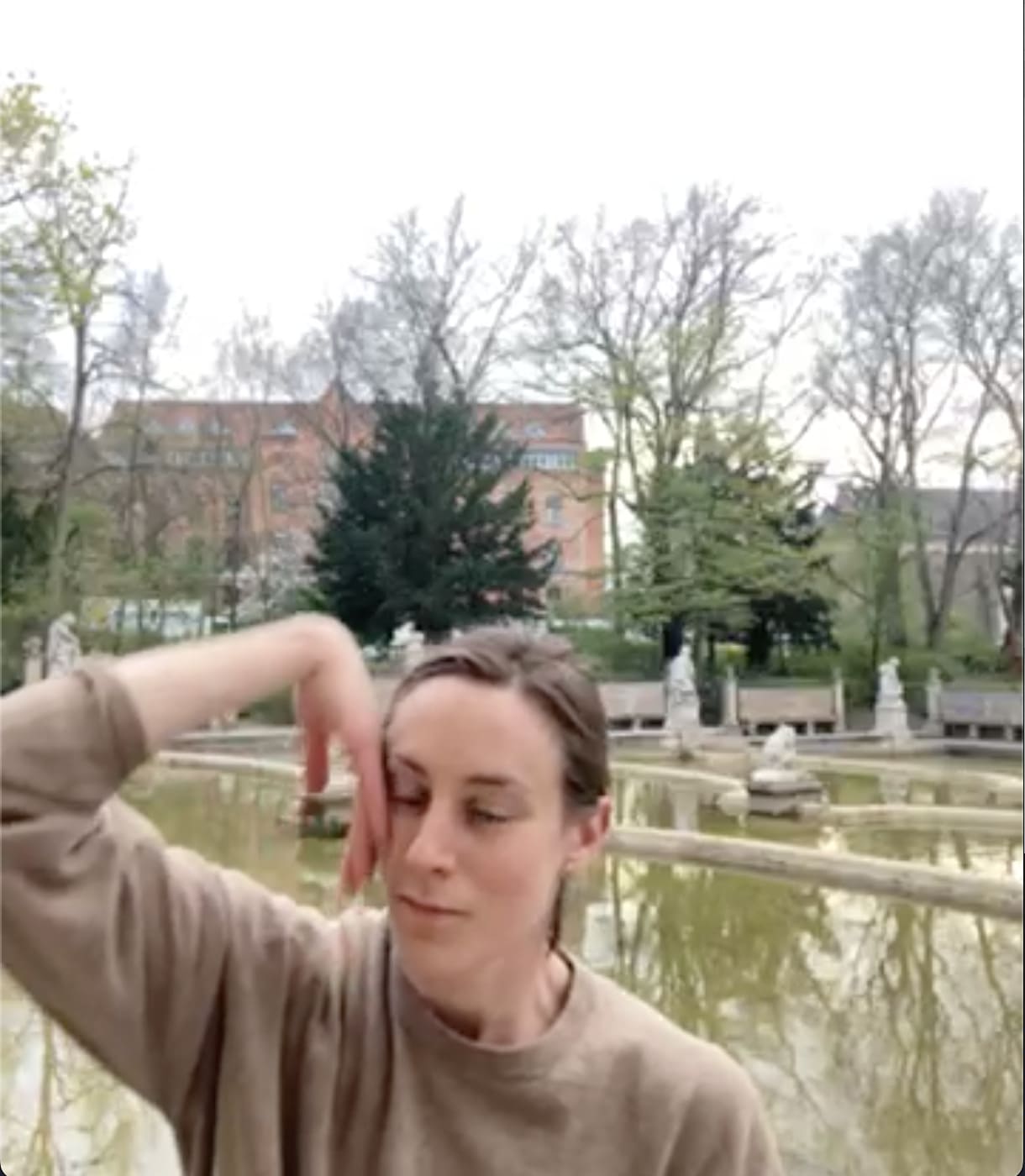 Person mit geschlossenen Augen vor der Wasserfläche eines Brunnens, sie berührt ihre Wange mit dem Handrücken
